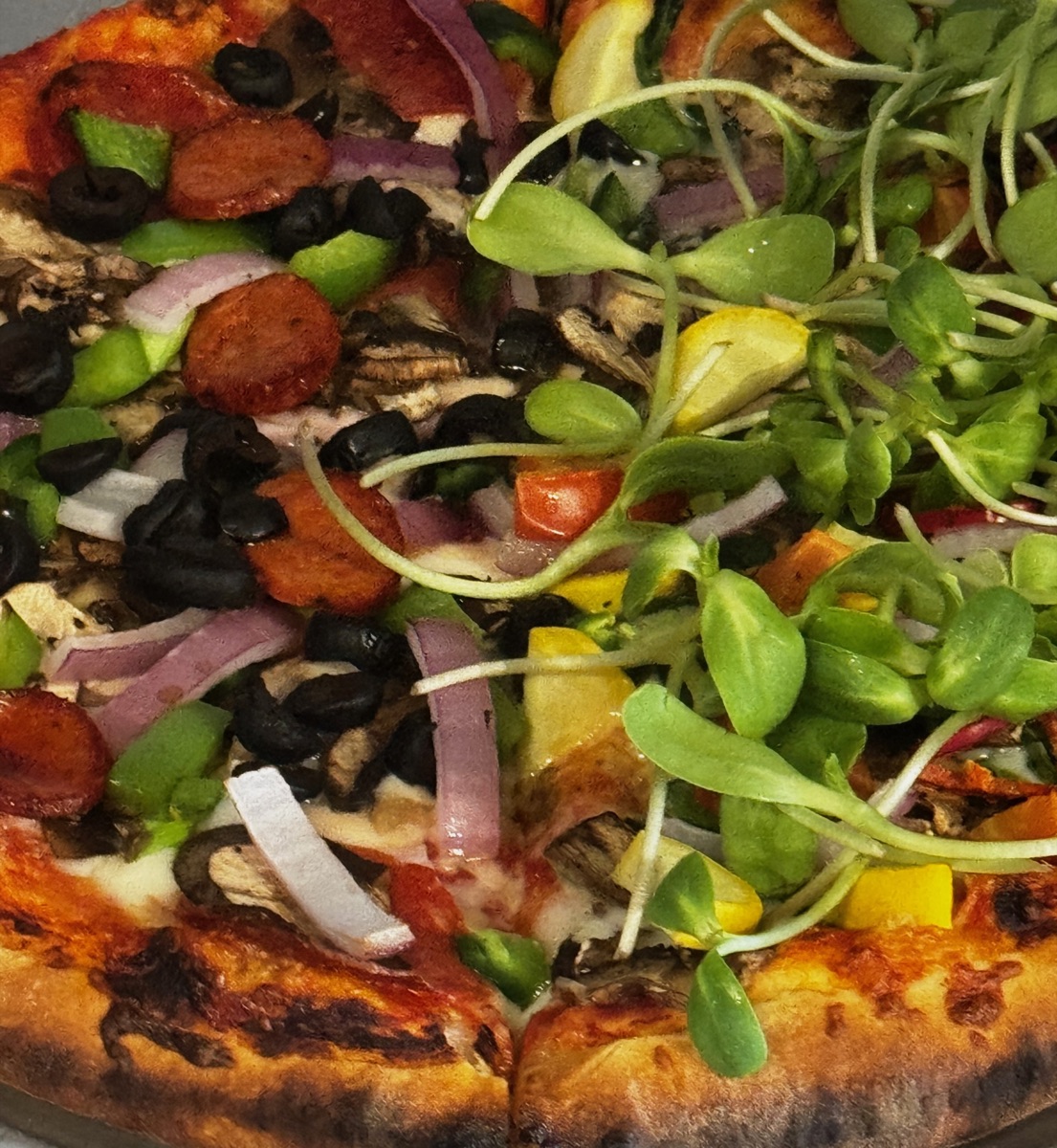 Close-up of a pizza with olives, peppers, onion, and fresh greens