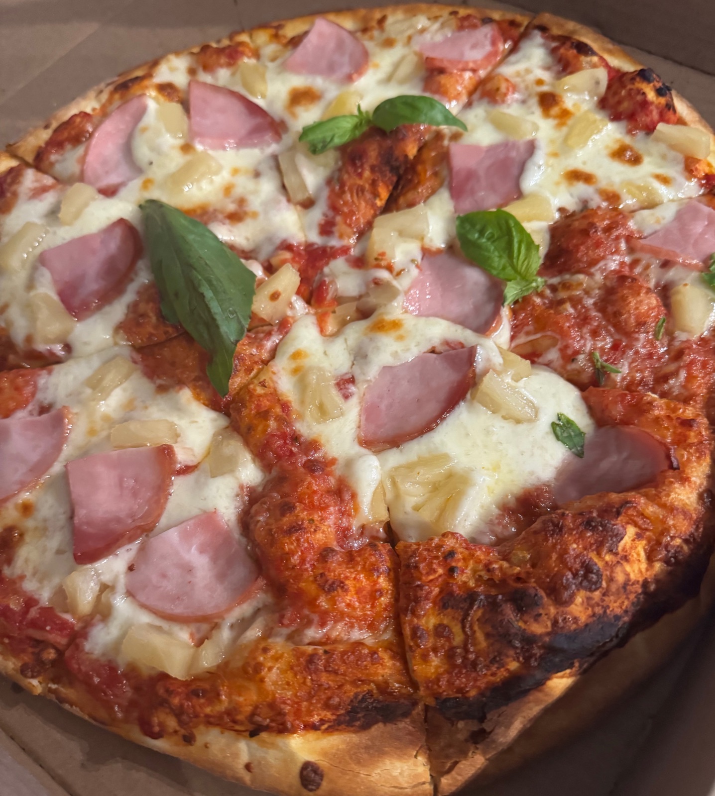 A Hawaiian pizza topped with ham, pineapple, and fresh basil