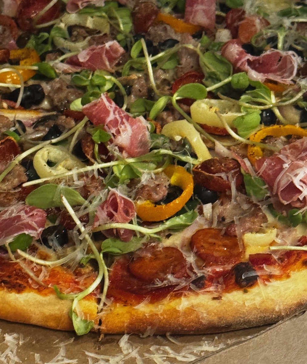 Close-up of a pizza with prosciutto, sausage, olives, and pepperoncini