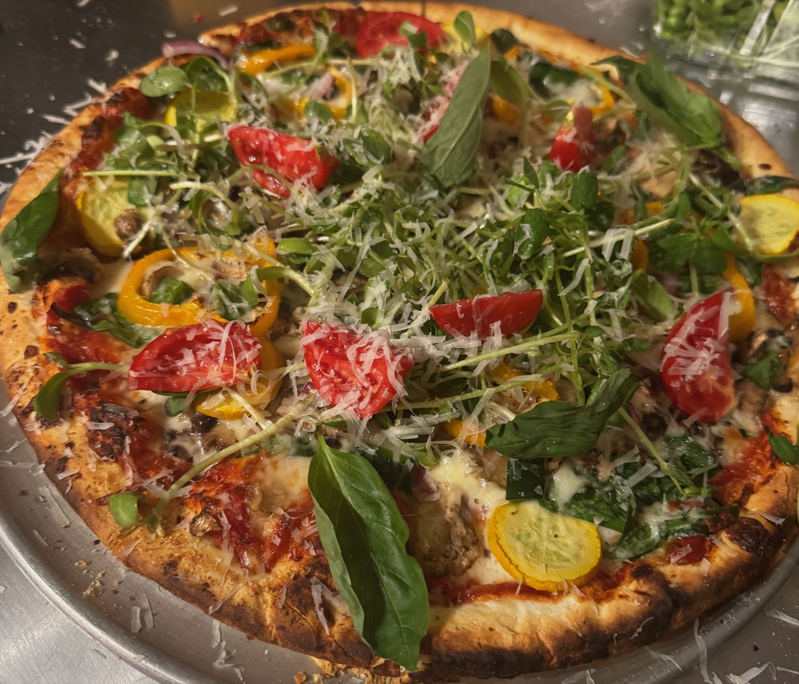 A pizza piled with peppers, tomatoes, squash, spinach, and fresh greens
